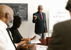 Senior executive conducting a business meeting with colleagues, discussing agenda on a whiteboard.
